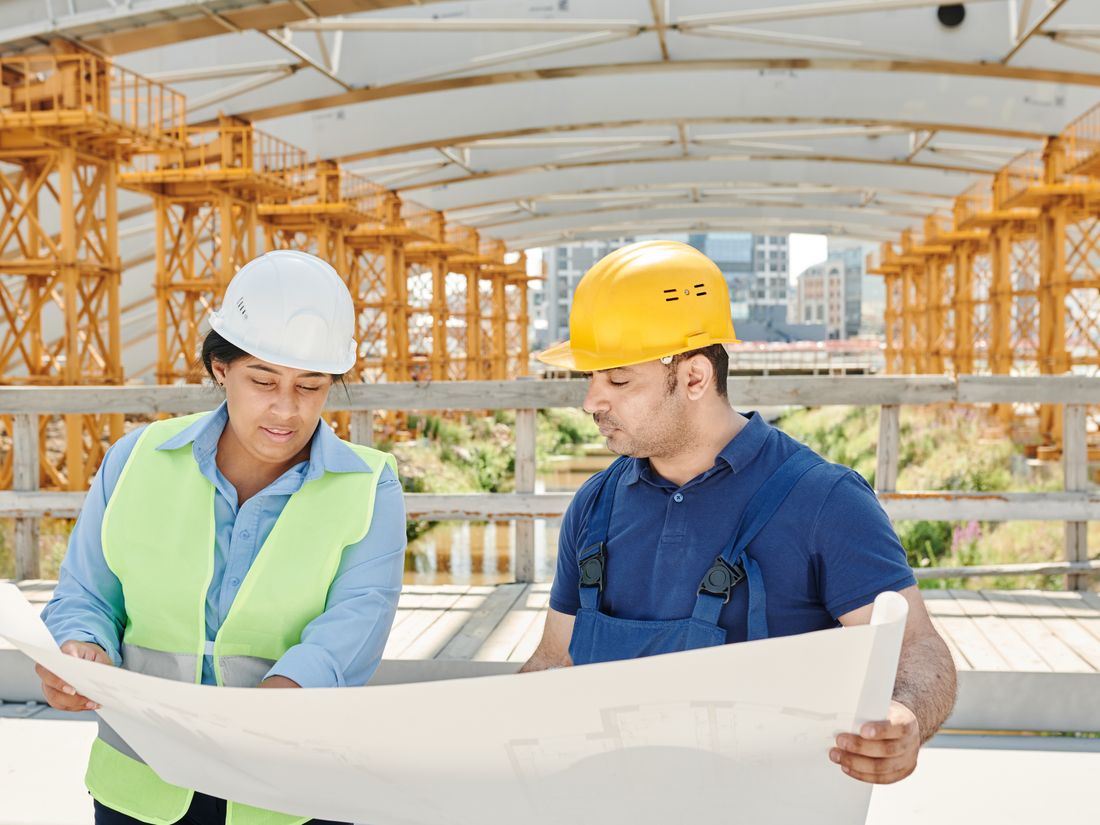 Two civil engineers in hard hats reviewing structural drawings at a construction site